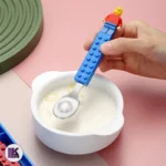 تصویری از ست قاشق و چنگال کودک با طرح لگو آبی و قرمز در حال استفاده